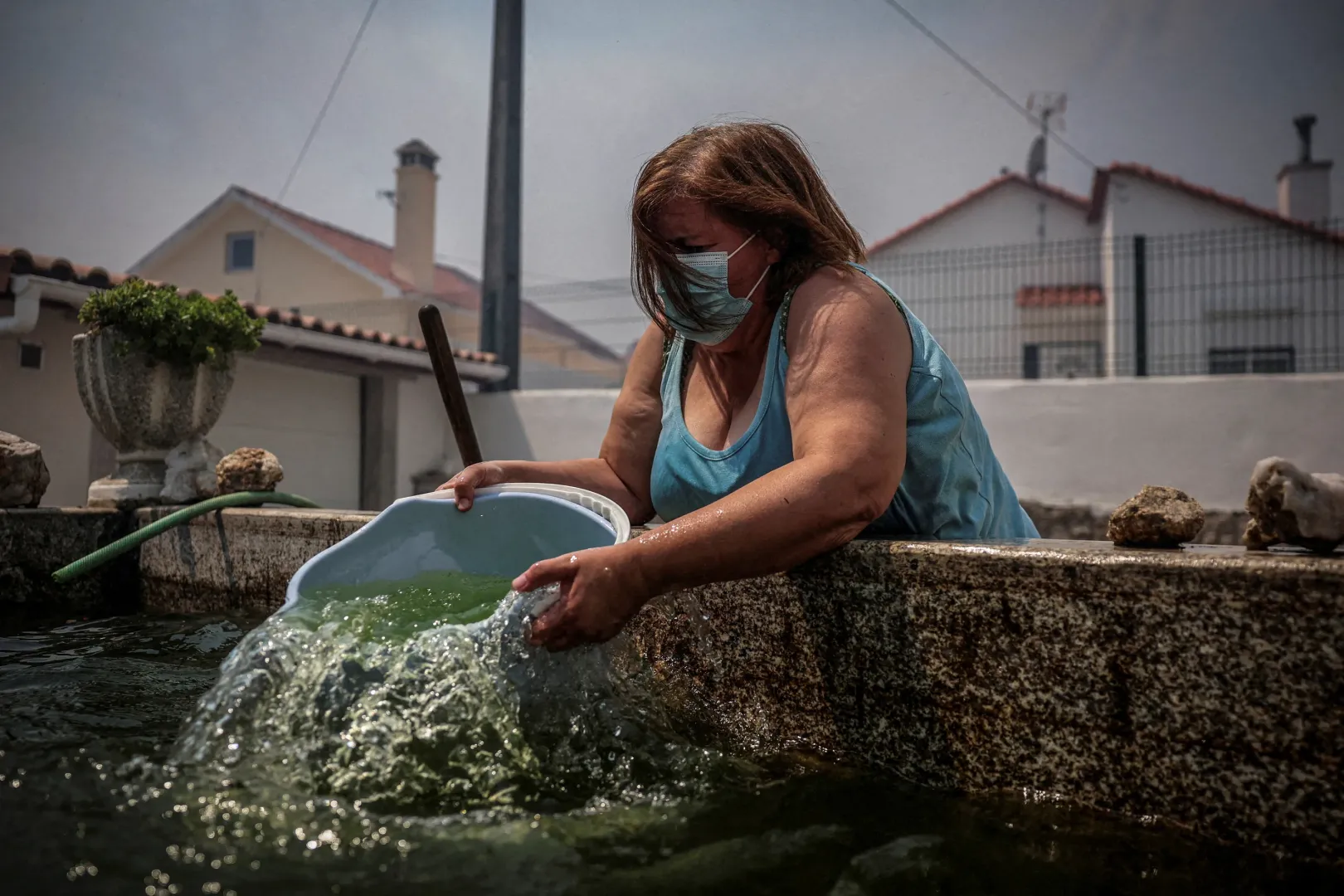 Egy nő vizet mer a vödörbe, miközben erdőtűz tombol a portugáliai Meda településen 2025. augusztus 15-én – Fotó: Pedro Nunes / Reuters