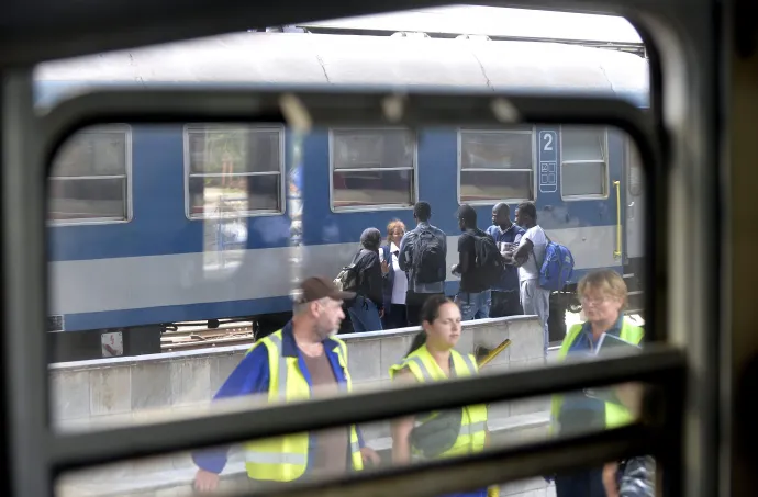 A B+N Referencia Zrt. takarítói várják a Szegedről érkező vonatot, miközben a háttérben bevándorlók útbaigazítást kérnek egy jegyvizsgálótól a Nyugati pályaudvaron a menekültválság idején 2015. július 30-án – Fotó: Máthé Zoltán / MTI