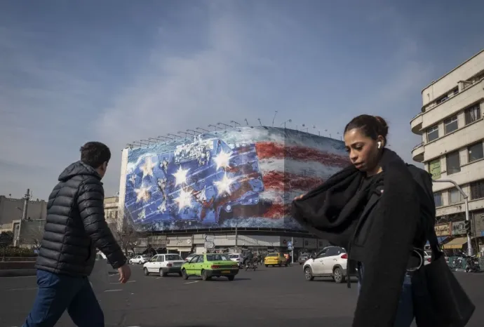 Járókelők az Enghelab téren Teheránban, mögöttük egy amerikai repülőgép-hordozót és az Egyesült Államok zászlaját ábrázoló molinó látható, 2026. január 25-én – Fotó: Morteza Nikoubazl / NurPhoto / AFP