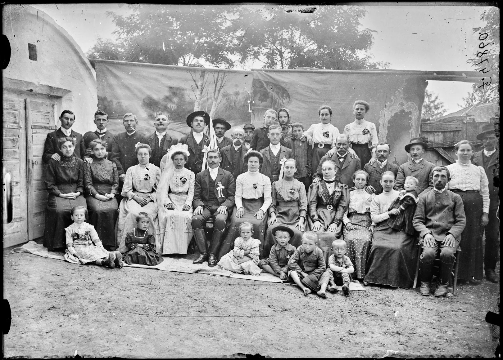 Lakodalmi csoportkép, a pincelejáró mellé rögzített két összeillesztett, festett háttér előtt. Devecser, 1910-es évek – Fotó: Néprajzi Múzeum Fényképtára / Siklós Géza felvétele