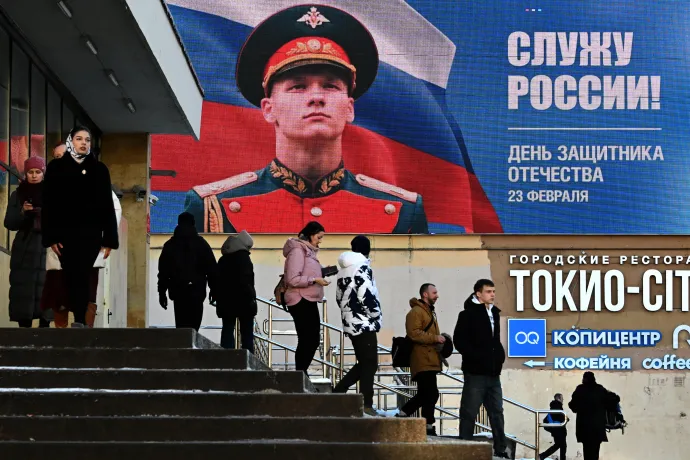 Emberek sétálnak el egy digitális képernyő előtt, amelyen egy orosz katona képe látható az „Oroszországot szolgálom!” szlogennel, a Haza Védelmezőinek Napján, Szentpéterváron, 2026. február 23-án – Fotó: Olga Maltseva / AFP