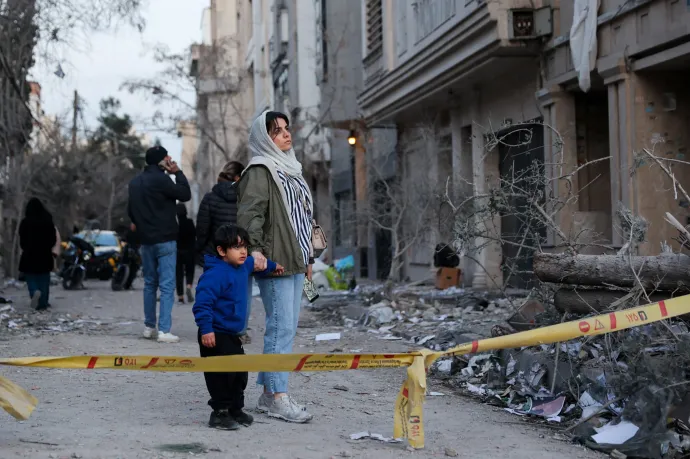 Egy nő gyermekével nézi, ahogy takarítják egy rendőrőrs romjait Teheránban egy amerikai légitámadást követően – Fotó: Majid Asgaripour / WANA / Reuters