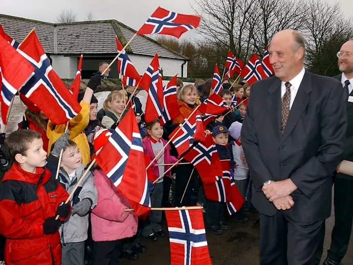 Egy skóciai általános iskola diákjai zászlókkal integetve üdvözlik V. Harald norvég királyt 2002-es látogatásán, illetve Harald a „Sira” nevű vitorlásán a Bodeni-tó partjánál, Dél-Németországban egy 2018-as versenyen – Fotó: Ian Stewart és Felix Kästle / AFP